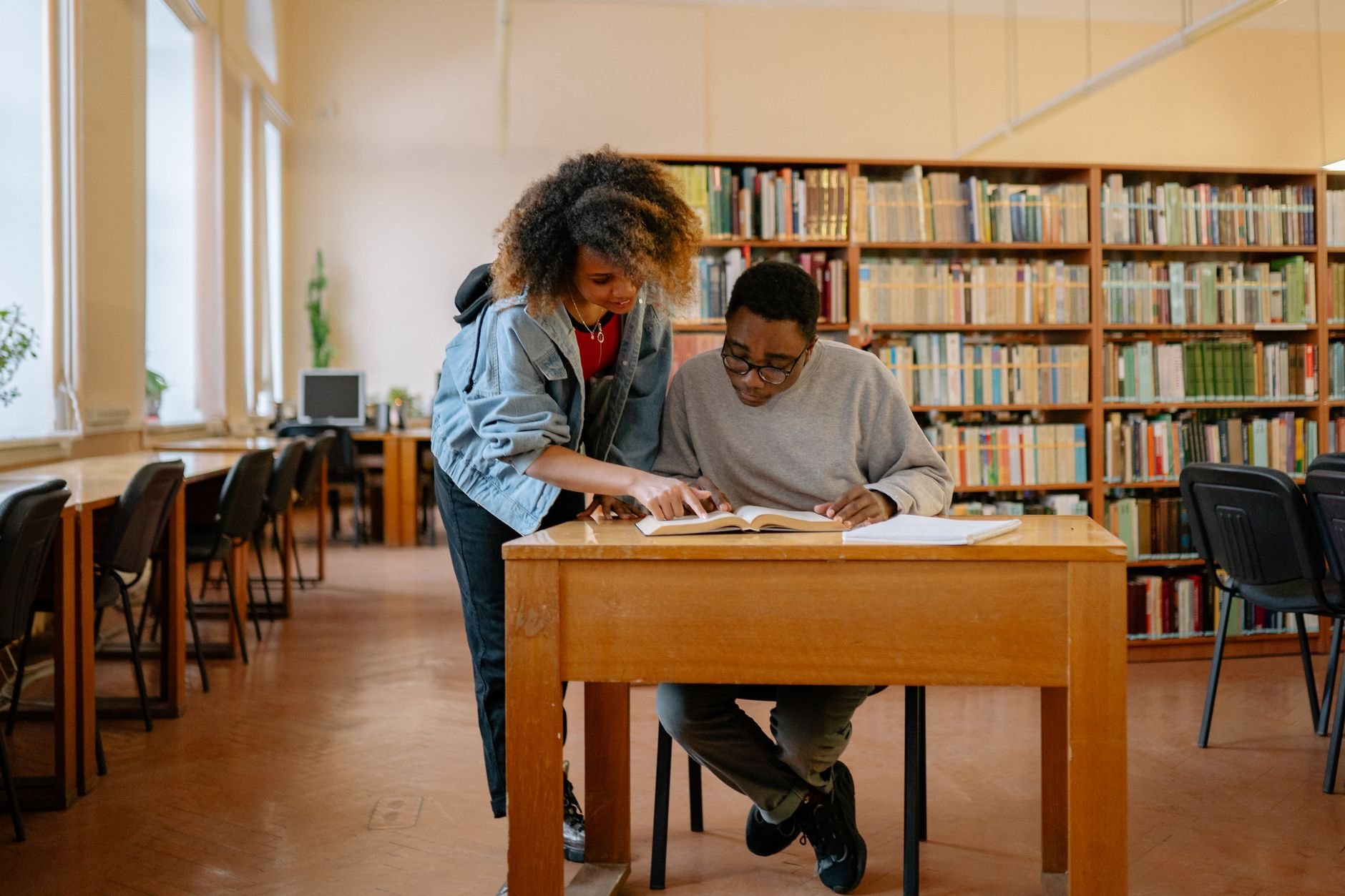 Two students engage in studying together at a library, surrounded by books and a peaceful atmosphere